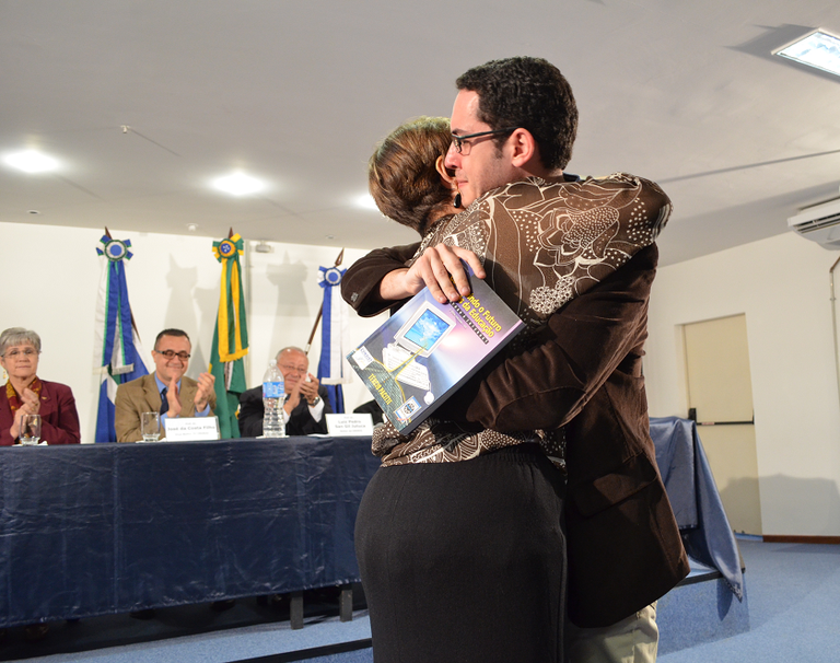 Eunice Pacitti entrega ao discente Arthur um livro do professor homenageado (Foto: Comso)