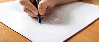 Close-up das mãos de um estudante escrevendo com caneta sobre papel branco.